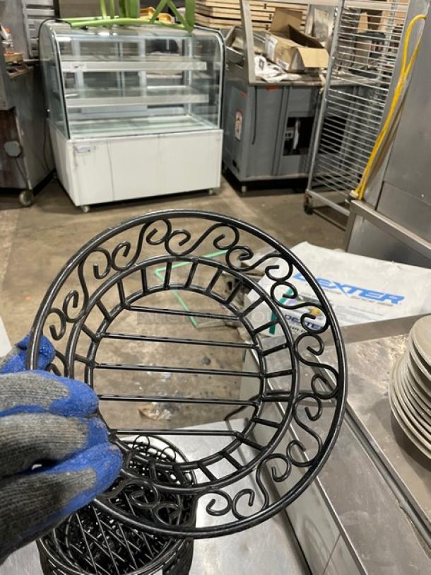 Black round wired basket with ornate swirl pattern, used condition, commercial setting. Measures approximately 9 inches in diameter.