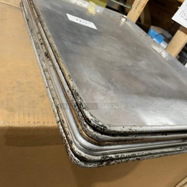 Commercial aluminum full-size sheet pans, stacked. Used condition with visible wear. Auction label reads "7X Your Bid."