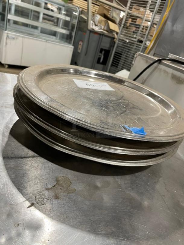 Stack of commercial stainless steel plates on a metal surface. Visible wear, label indicating lot number. Auction item.