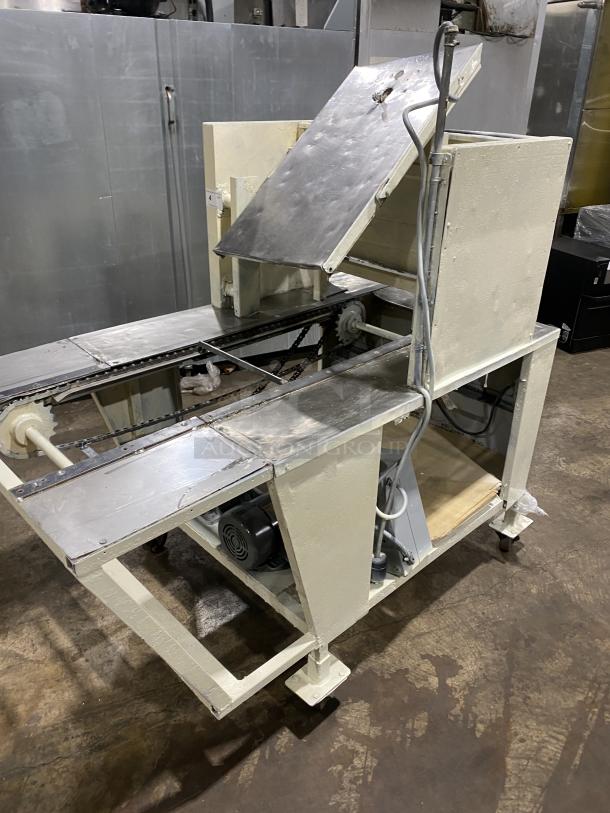 Commercial stainless steel dough sheeter machine, robust and industrial-grade. Visible motor and conveyor system, in used condition.