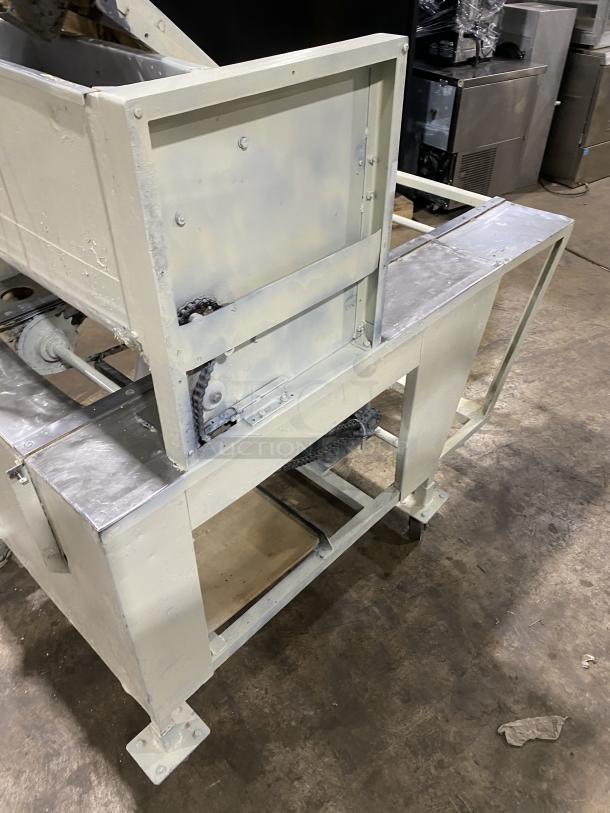 Commercial stainless steel dough sheeter machine, industrial-grade, visible wear, chain mechanism, mounted on sturdy frame.