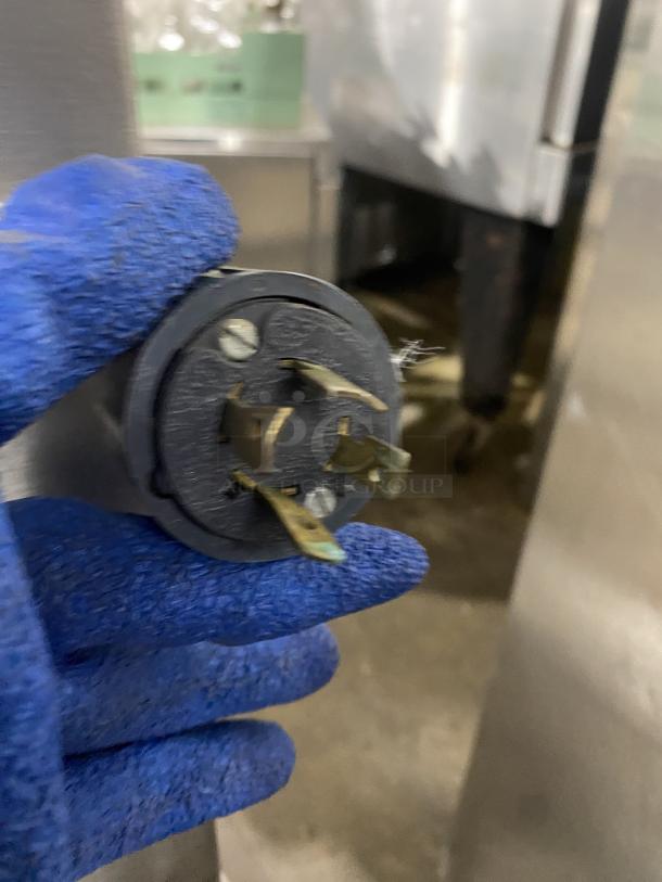 Blurry image showing electric plug component held by gloved hand, likely part of Minipan commercial dough sheeter.