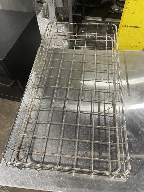 Commercial stainless steel wired bagel basket on stainless surface, showing mild rust and wear.