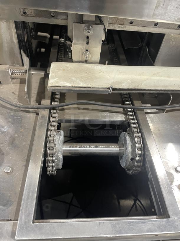 Aksar commercial tray wrapping machine, floor style, heavy-duty design, visible chain mechanism, model URL: aksarfoodmachine.com.