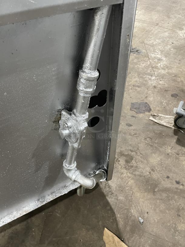 A close-up of a metal pipe connection on a Jade Range gas-powered 4 burner/char broiler combo, showing casters.