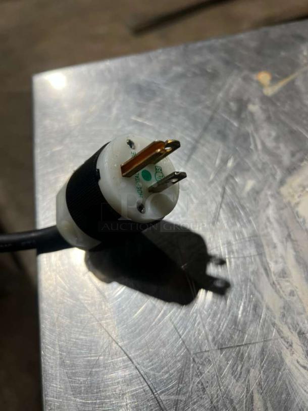 A close-up of a plug for a Traulsen AHT2-32 refrigerator, showing a three-prong design on a metallic surface.