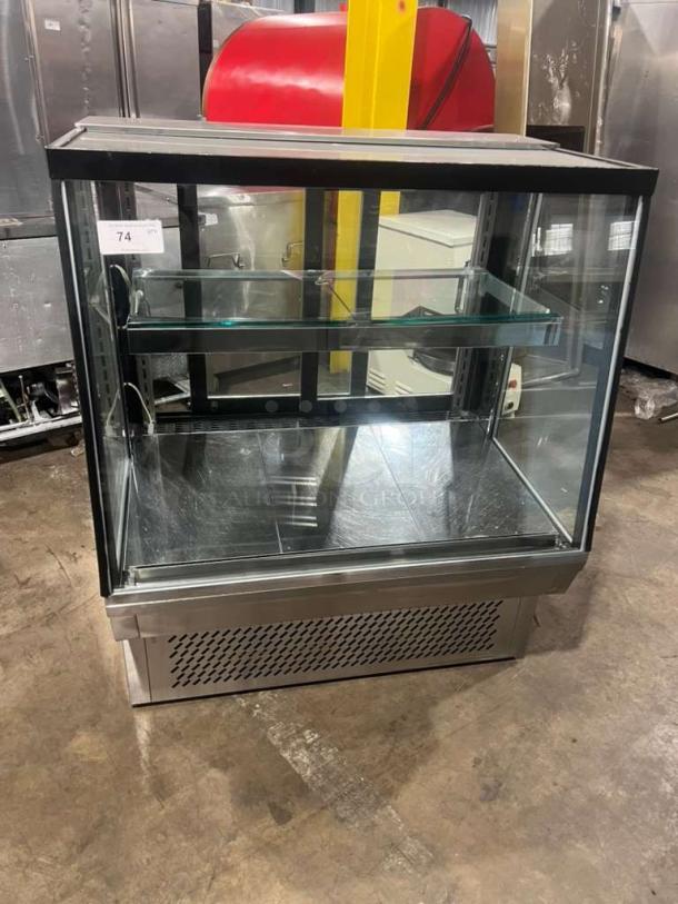 Custom Cool refrigerated bakery display case with glass shelves and stainless steel base. Excellent condition. Auction tag shows "74 QTY."