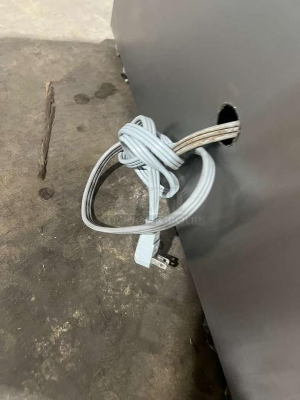 Custom Cool Refrigerated Bakery Display Case power cord extending through rear panel, shown on concrete floor.