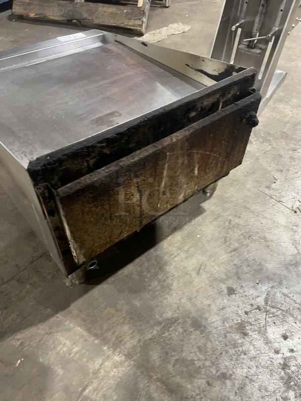 Commercial stainless steel gas griddle with back and side splash, on legs. Shows signs of use, ideal for high-volume cooking.