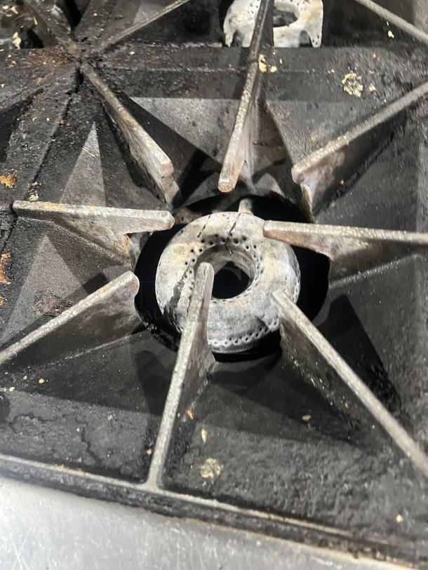Close-up of a Vulcan stainless steel burner, part of an 8-burner range. Shows signs of use with some residue visible.