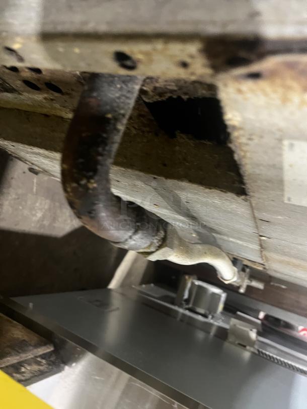 Blurred image of a pipe and underside of a Vulcan commercial range, showing some rust and metal wear.