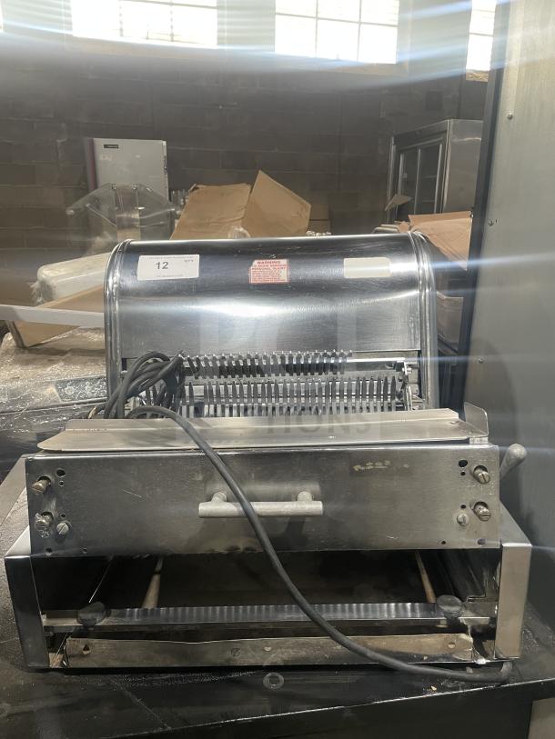 Berkel commercial stainless steel countertop bread slicer in used condition. Features include serrated blades and control knobs. Markings: Quantity label "12" and warning sticker visible.