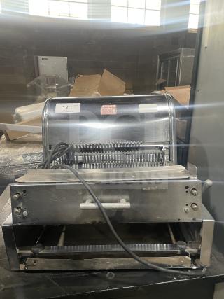 Berkel commercial stainless steel countertop bread slicer in used condition. Features include serrated blades and control knobs. Markings: Quantity label "12" and warning sticker visible.