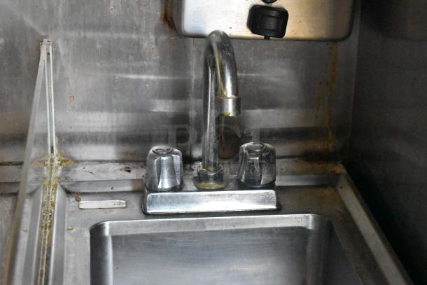 Stainless steel sink with dual-handle faucet in 2019 Quality Cargo mobile kitchen trailer, moderate wear visible.