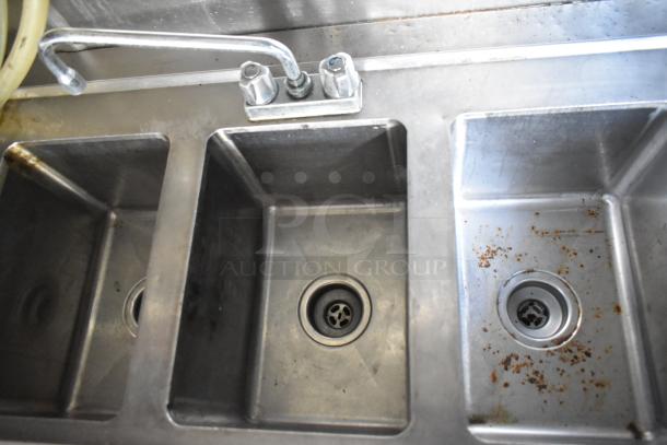 Triple stainless steel sink with faucet in mobile kitchen trailer, shows wear and rust spots, part of 2019 Quality Cargo unit.