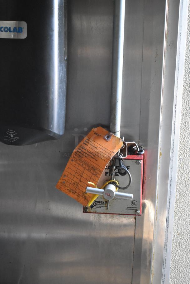 Fire suppression system handle with inspection tag inside a mobile kitchen trailer. Tag shows operational details.