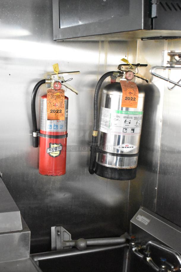 Two mounted fire extinguishers, visible labels reading "2022" and brand logos, inside mobile kitchen trailer.