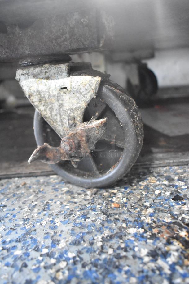 Old, rusted caster wheel on a rough, speckled blue and gray flooring. Close-up view highlights corrosion.