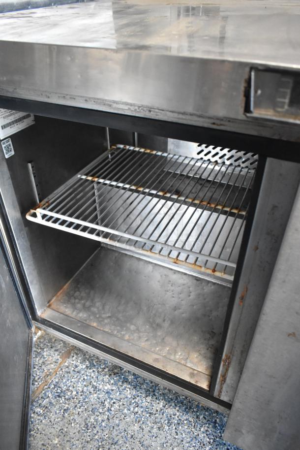 Rusty metal interior of a refrigeration unit with a wire shelf, part of a 2019 mobile kitchen trailer.