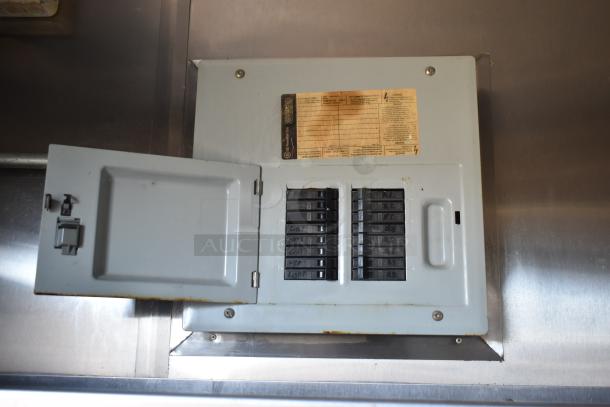 Electrical panel of the 2019 Quality Cargo Mobile Kitchen Trailer with labeled circuit breakers, mounted on stainless steel wall.