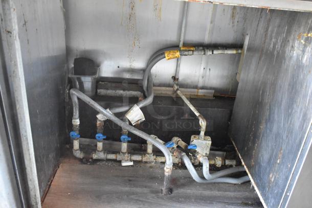 Rusted piping and connections inside the 2019 Quality Cargo mobile kitchen trailer, visibly aged with some corrosion.