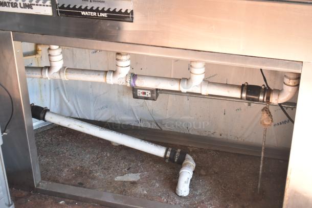 Under-sink plumbing of 2019 Quality Cargo mobile kitchen trailer. Visible PVC pipes and electrical outlet.