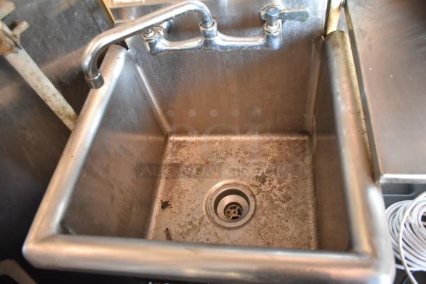 Stainless steel sink in mobile kitchen trailer, showing wear and use. Features wall-mounted faucet and visible drain.