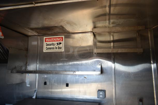 2019 Quality Cargo 8.5' x 24' mobile kitchen trailer interior with stainless steel walls, "Warning: Security Cameras In Use" sign, and outlet.