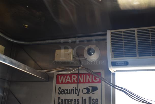 Interior of a mobile kitchen trailer showing an air conditioning unit, a security camera, and a "Warning: Security Cameras In Use" sign.