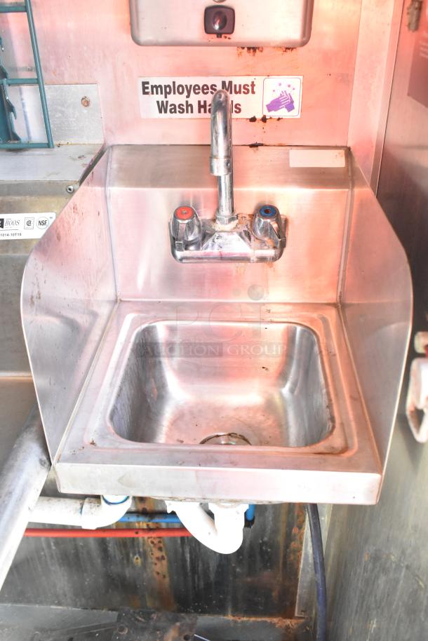 Stainless steel sink with hot and cold faucets, located in a mobile kitchen trailer, featuring "Employees Must Wash Hands" signage.