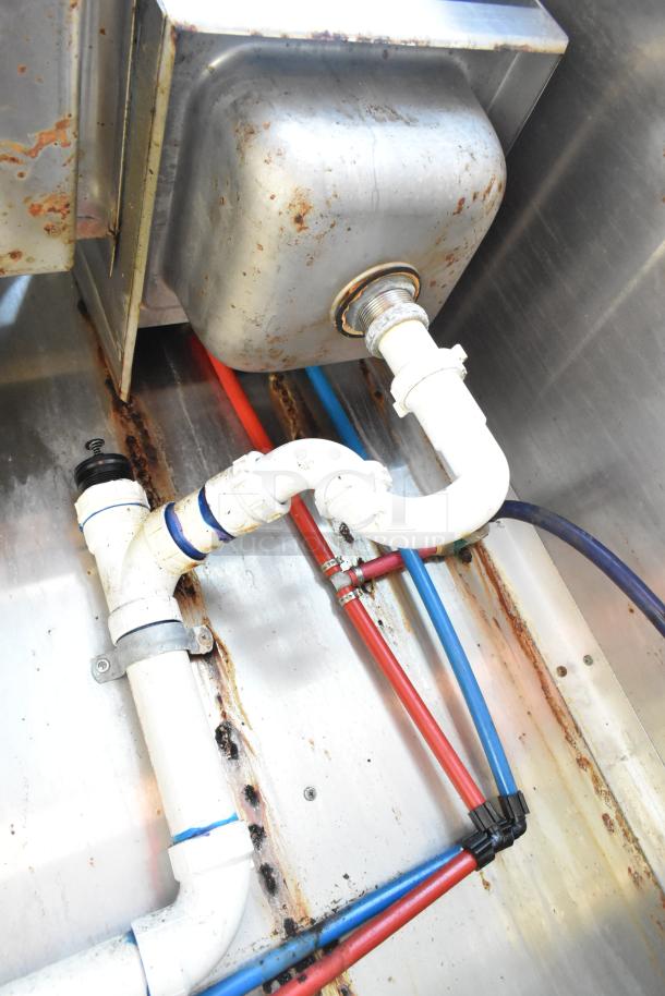 Close-up view of plumbing setup in 2020 Diamond Cargo mobile kitchen trailer, showing metal sink and colored pipes. Some rust visible.