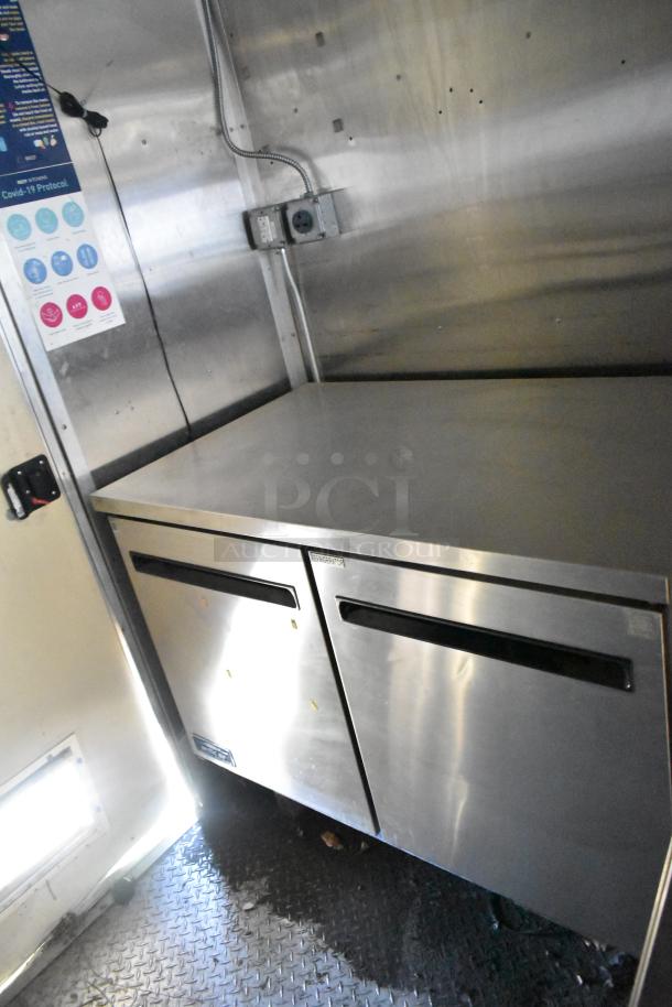 2020 Diamond Cargo 8.5' x 24' mobile kitchen trailer interior with stainless steel refrigerator, electrical outlets, and safety signage.