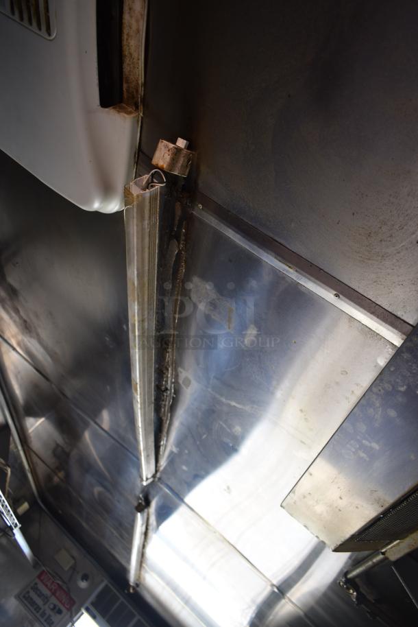Interior view of a 2012 Quality Cargo food trailer, showcasing stainless steel surfaces and ceiling fittings. Signs of wear visible.