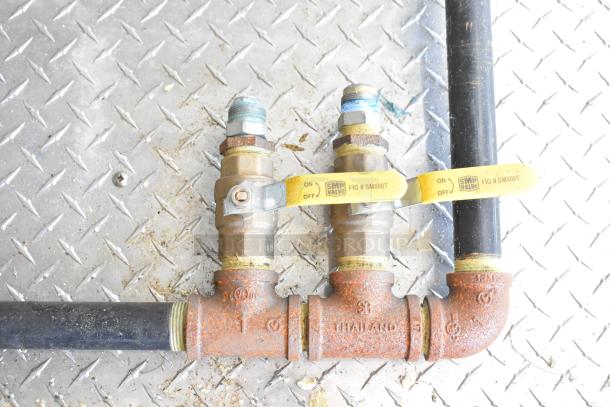 Rusted plumbing valves on a diamond plate surface, featuring SMP Valve tags with "FIG # SM600T" and "ON/OFF" markings.