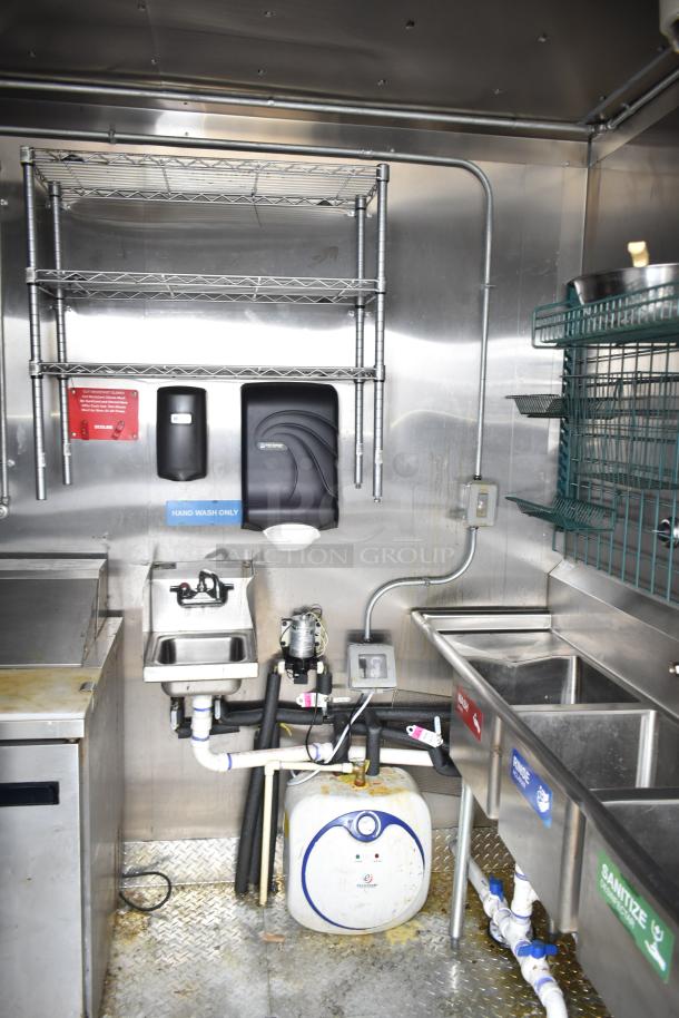 Interior of 2021 Diamond Cargo mobile kitchen trailer showing stainless steel sink setup, plumbing, metal shelves, and sanitizer station.