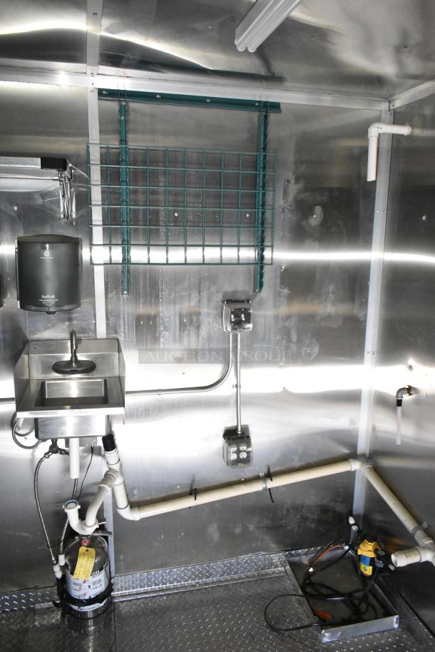 Interior view of a 2021 Diamond Cargo kitchen trailer, featuring a stainless steel sink, electrical outlets, and plumbing setup.