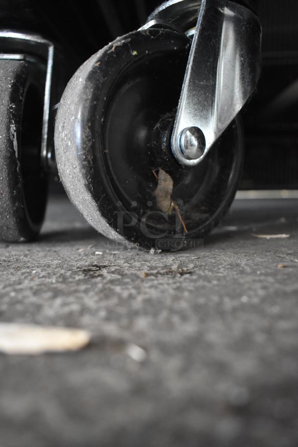 Close-up of commercial caster wheel on a True T-49F-HC cooler. Visible wear and debris on floor.