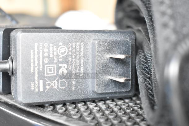 Close-up of a black switching power adapter, model GS-120200BHU, with visible safety markings and specifications.