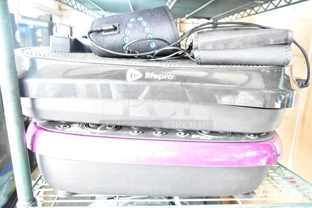Two LifePro vibrating plates, black and purple, with accessories, on a metal shelf. Good condition, LifePro logo visible.