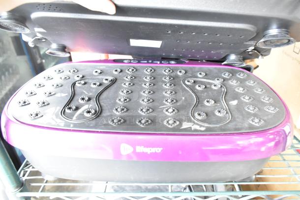 LifePro vibrating plate in purple with textured black footpad, used condition, front logo visible, placed on a metal shelf.