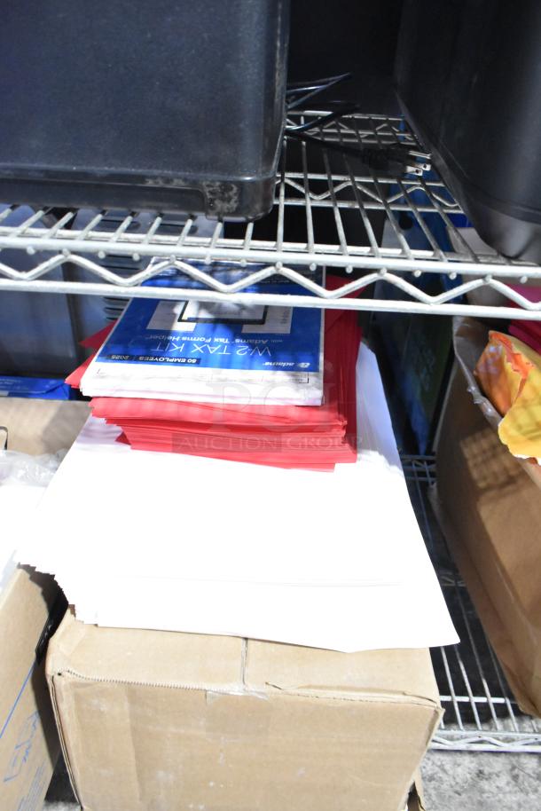 Tier lot of items on metal shelf, including a stack of exam table paper, red and white file folders, and assorted boxes.