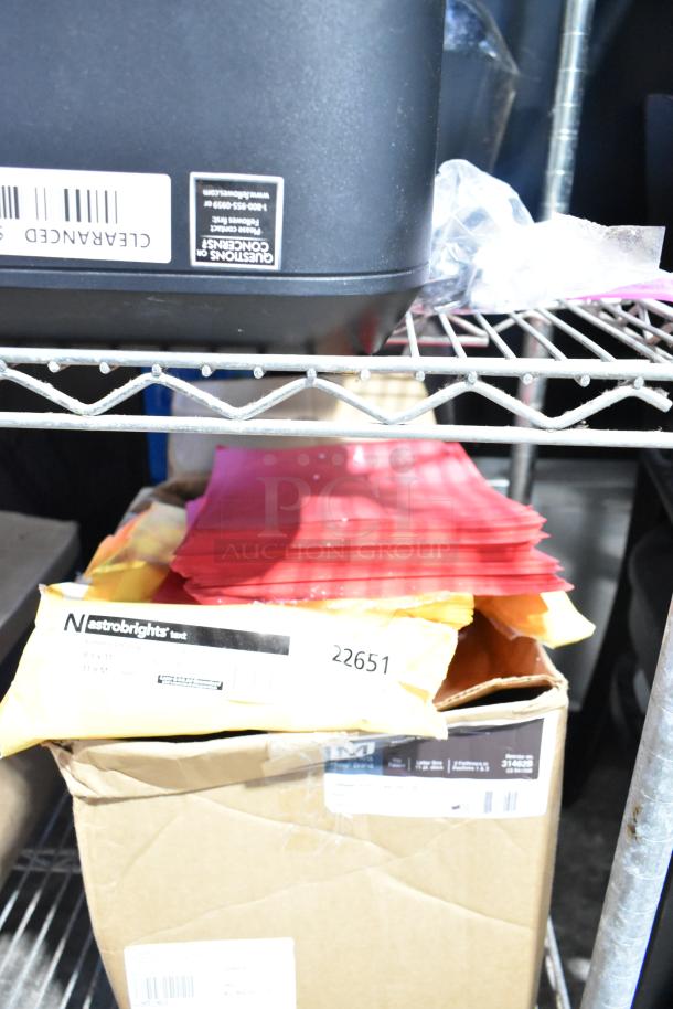Auction tier lot with Astrobrights paper, red folders, boxes, and plastic wrap, stacked on a metal shelf.