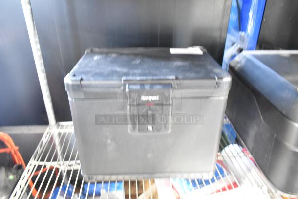 Honeywell black safe, visible brand logo, sturdy design, no key included, good condition, stored on metal shelf.