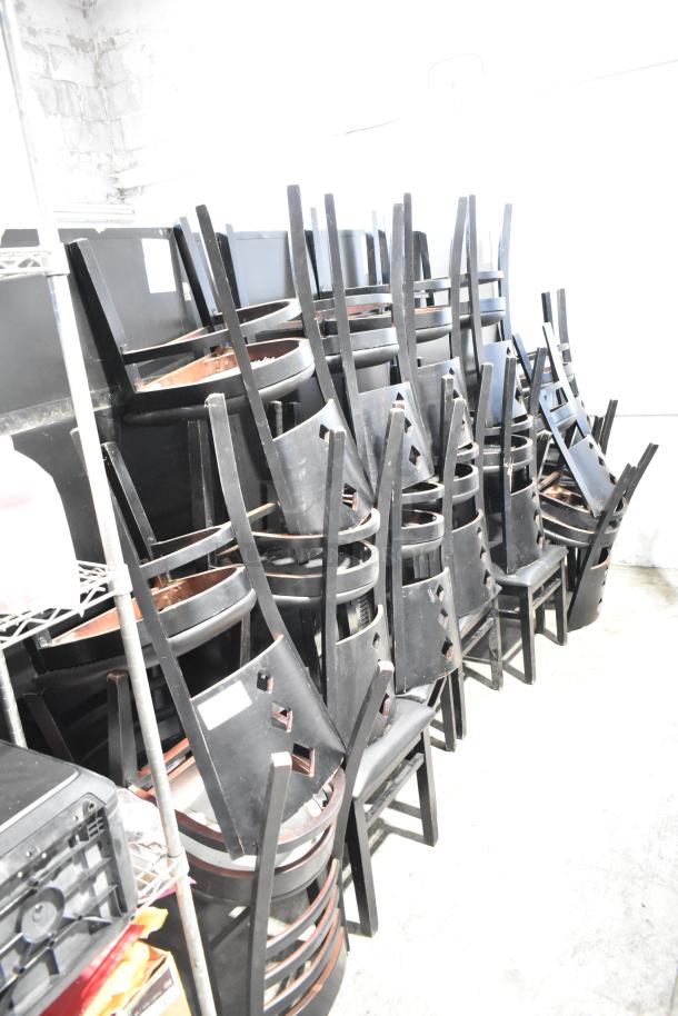 21 various black dining height chairs with black seat cushions stacked in a storage area; condition appears used.