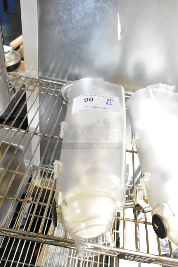 Two clear poly dry food dispenser hoppers on a wire shelf, labeled "90 QTY x2" by PCIAuctions.com.