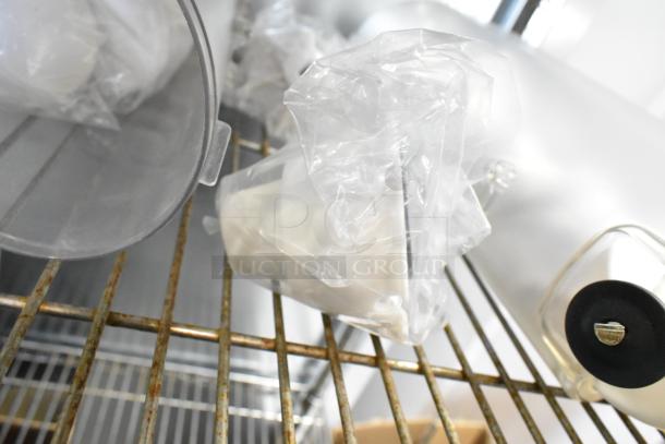 Two clear poly dry food dispenser hoppers on a metal shelf, unused and wrapped in protective plastic.