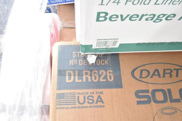 Boxes of new scratch and dent items including napkins, guest towels, food bags. Visible labels: Dart Solo, Made in USA.