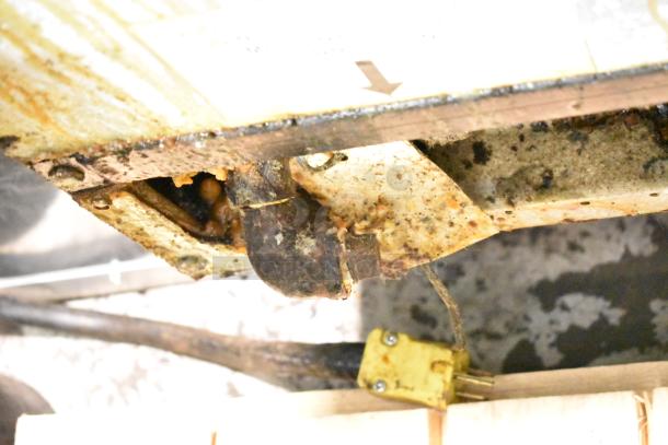 Close-up of Frymaster BIGLA330-6CSD fryer's underside, showing corroded and greasy parts. Natural gas connections visible.