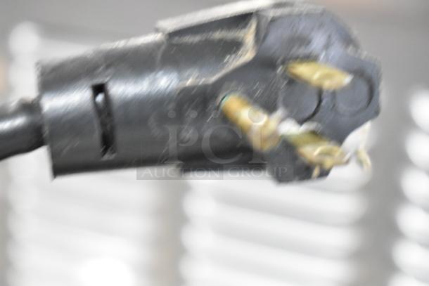 Blurry image of a black electrical plug with three prongs, part of a commercial ice cream dipping cabinet, 115 volts, 1 phase.