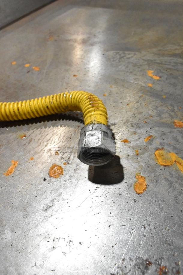Close-up of a yellow gas hose and connector for a Commercial Countertop Gas Powered Flat Top Griddle on a metallic surface.